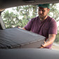 A man is opening a box containing the Deepsleep Solo Mat for Subaru Outback by CarToCamp in a car.