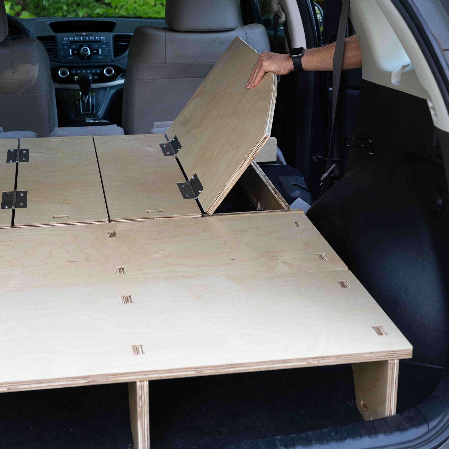 A person utilizing the storage space in a Honda CR-V to assemble a CarToCamp Sleeping Platform.