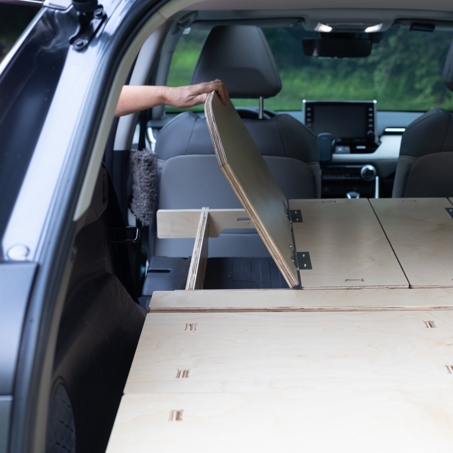 A person is opening the trunk of a CarToCamp Toyota RAV4 Sleeping Platform to access storage space.